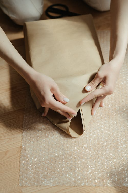 A person packaging a product in brown paper.