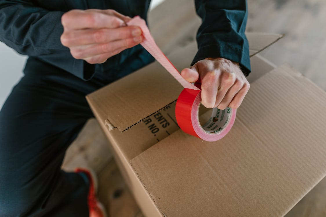 A person wrapping red colored tape on a box.